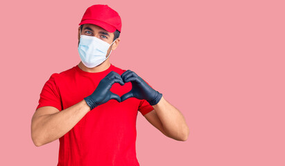 Fototapeta na wymiar Young hispanic man wearing covid-19 safety mask smiling in love showing heart symbol and shape with hands. romantic concept.