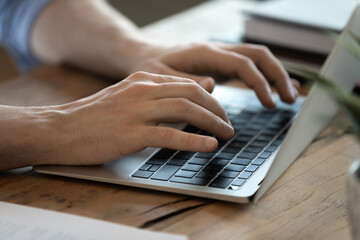 Man using wireless computer seated at workplace desk. Male hands typing letter e-mail close up view...