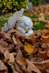 A small statue of a young angel sleeps among the fallen autumn leaves in a cemetery in Niagara on the Lake, Ontario.