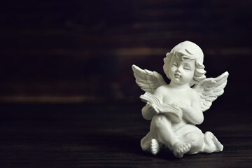 Guardian angel sitting and holding a book on dark background with copy space