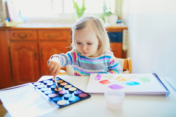 Adorable little girl drawing with colorful aquarelle paints