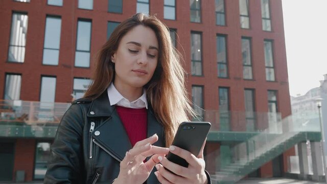 attractive young female serfing internrt news make bought online and typing text on smartphone and smilling near city buildings. Close-up of full 360 degree rotation. Tracking Arc Shot 4k