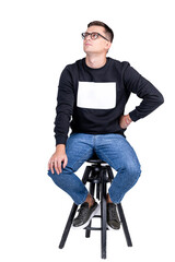 Model man presents modern glasses. Male sits on high bar chair in casual sweater and blue jeans.