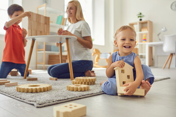 Happy family mother and children playing with wooden toy details at home together