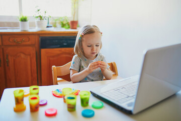 Toddler girl playing modelling clay in front of laptop