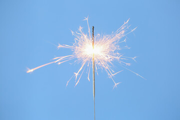 Bright burning sparkler on light blue background, closeup