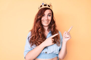 Young beautiful woman wearing princess crown smiling and looking at the camera pointing with two hands and fingers to the side.