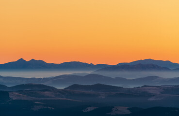 Beautiful, colorful mountain landscape in orange and blue tones with morning fog at sunrise.