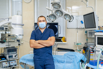 Obraz premium Portrait of a male surgeon in mask standing arms crossed in operation room. Professional and confident doctor.