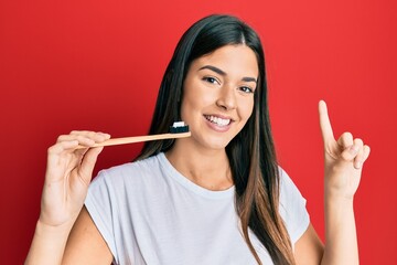 Young brunette woman holding toothbrush with toothpaste smiling with an idea or question pointing finger with happy face, number one