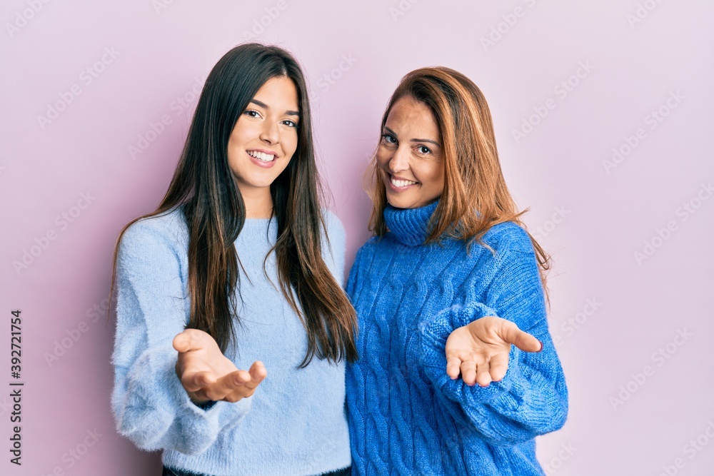 Sticker Hispanic family of mother and daughter wearing wool winter sweater smiling cheerful offering palm hand giving assistance and acceptance.