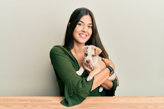 Young hispanic girl smiling happy and hugging dog sitting on the table over isolated white background.