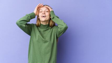 Young blonde woman isolated on purple background laughs joyfully keeping hands on head. Happiness concept.