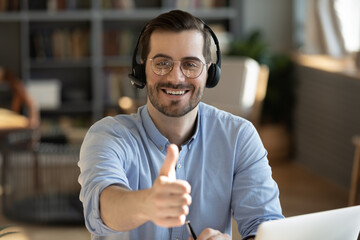 Man wear headset sit at desk look at camera show thumbs up advise quality distant training, advertising foreign language online educational course, easy comfort knowledge improvement using modern tech