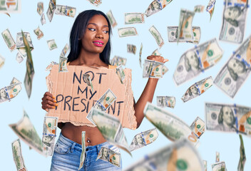 Young african american woman holding not my president protest banner pointing thumb up to the side smiling happy with open mouth