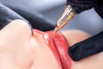 Applying red pigment with tattoo machine on woman lips, permanent makeup in beauty salon - obrazy, fototapety, plakaty