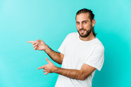 Young man with long hair look excited pointing with forefingers away.