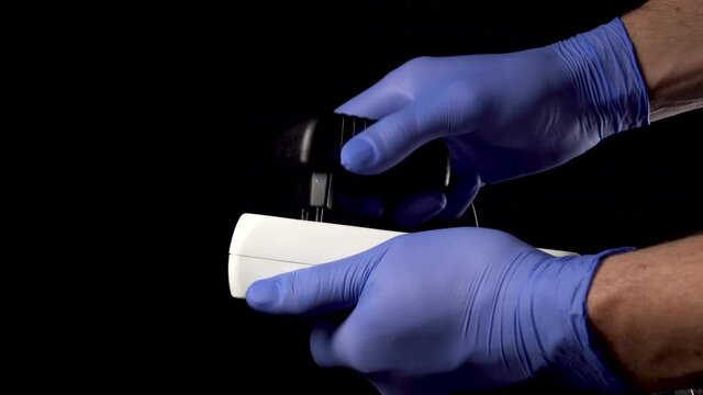Doctor disconnects the plug of the medical device from the electrical outlet. In blue medical protective surgical gloves on a black background. Close-up. Euthanasia concept