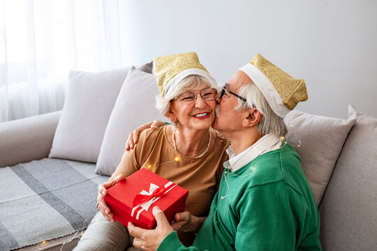 Senior couple exchanging presents at Christmas time indoors. Christmas, New Year, Celebration, Holiday-event. Senior couple celebrating Christmas at home, exchanging Christmas presents