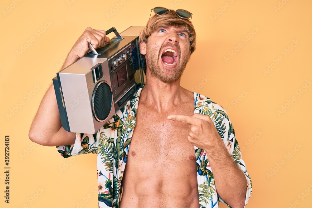 Poster young blond man wearing summer style holding boom box angry and mad screaming frustrated and furious