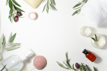 Obraz na płótnie Canvas Spa and beauty. A set of natural cosmetics. Soap, cream, white towel, sponge and olive tree sprigs are arranged around the perimeter on a white background. Copy space.