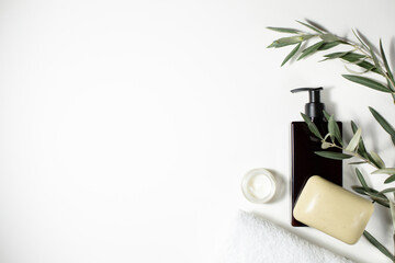 A black jar with a dispenser, a white towel, soap, a sprig of an olive tree are on a gray...