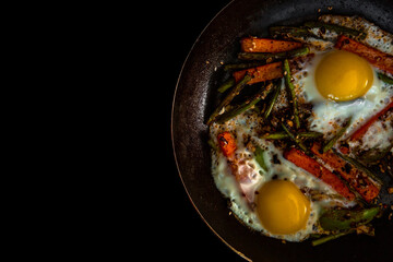 Fototapeta na wymiar Two fried eggs in a pan with large slices of carrots, bell pepper and asparagus with spices and sauce. Close.