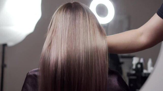 Master hairdresser combs the beautiful hair of a female client after the dyeing procedure. Back view, close-up.
