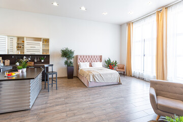 Contemporary ordinary design of spacious studio in soft warm colors. Simple furniture. Light large room with sunlight. Daytime. Tiled brown floor and white walls .