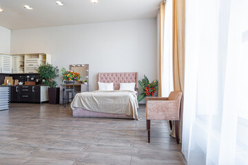 Contemporary ordinary design of spacious studio in soft warm colors. Simple furniture. Light large room with sunlight. Daytime. Tiled brown floor and white walls .