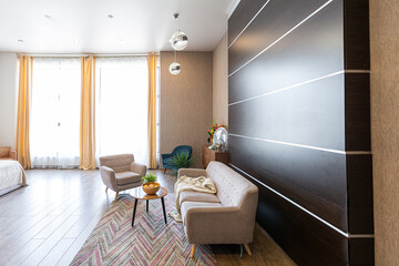 Contemporary ordinary design of spacious studio in soft warm colors. Simple furniture. Light large room with sunlight. Daytime. Tiled brown floor and white walls .