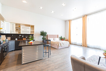 Contemporary ordinary design of spacious studio in soft warm colors. Simple furniture. Light large room with sunlight. Daytime. Tiled brown floor and white walls .