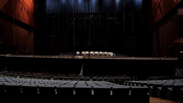 Empty rows of armchairs in a dark hall for a conference or a forum. Media. Empty concert hall before mass public event with a lot of empty chairs and comfortable beige armchairs on the stage.