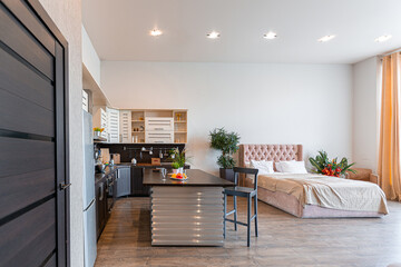 Contemporary ordinary design of spacious studio in soft warm colors. Simple furniture. Light large room with sunlight. Daytime. Tiled brown floor and white walls .