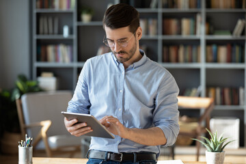 Focused serious businessman freelancer in glasses standing in modern office lean on table hold...