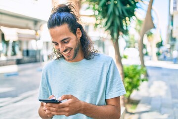 Young hispanic man smiling happy using smartphone at city.
