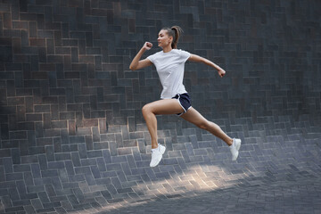 Fototapeta na wymiar Woman with fit body jumping and running against black wall background