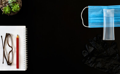 Medical surgical face mask for coronavirus protection, disinfectant gel, gloves, note block. Black background with copy space. Flat lay.