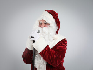 Santa Claus singing with microphone on light grey background. Christmas music