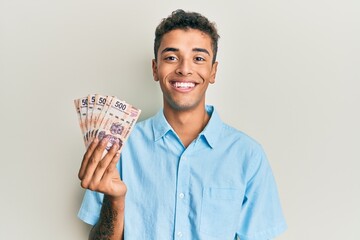 Young handsome african american man holding 500 mexican pesos banknotes looking positive and happy standing and smiling with a confident smile showing teeth