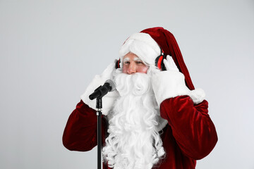 Santa Claus with headphones and microphone on light grey background. Christmas music