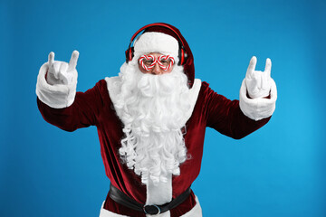 Fototapeta na wymiar Santa Claus with headphones listening to Christmas music on blue background