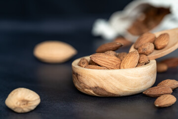 Almonds in a wooden bowl and on a wooden spoon on a black wooden table. some fruits are in a cotton mesh eco bag