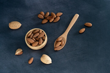 Almonds in a wooden bowl and on a wooden spoon on a black wooden table. top view
