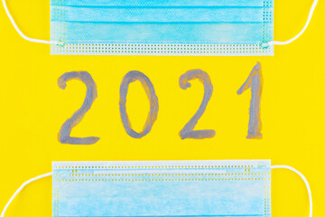 Text 2021 on a yellow background and surgical mask. Concept of the New Year with blue protective...