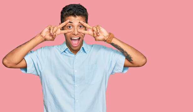 Young handsome african american man wearing casual clothes doing peace symbol with fingers over face, smiling cheerful showing victory
