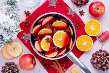 Cooking mulled wine with oranges, apples, anise and cinnamon for Christmas on pink table top, top view, flat lay