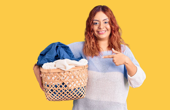 Young latin woman holding laundry basket smiling happy pointing with hand and finger