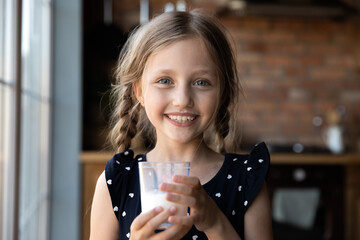 Tastes so good. Portrait of happy cheerful little girl holding glass of yoghurt looking at camera...