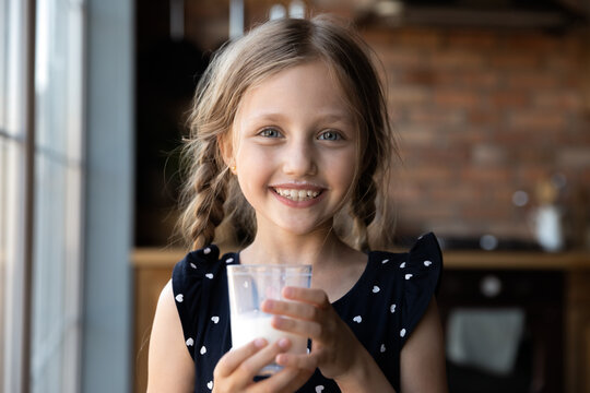 Tastes So Good. Portrait Of Happy Cheerful Little Girl Holding Glass Of Yoghurt Looking At Camera With Milk Mustache On Face, Cute Child Promotes Healthy Habit Drink Fresh Farm Dairy Product Every Day